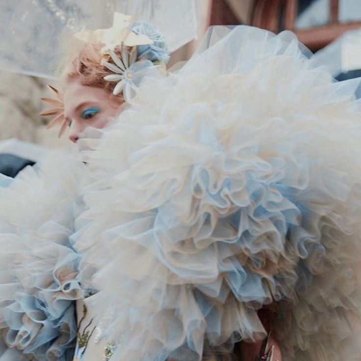 a woman in a blue and white dress with feathers on her head looking at the camera