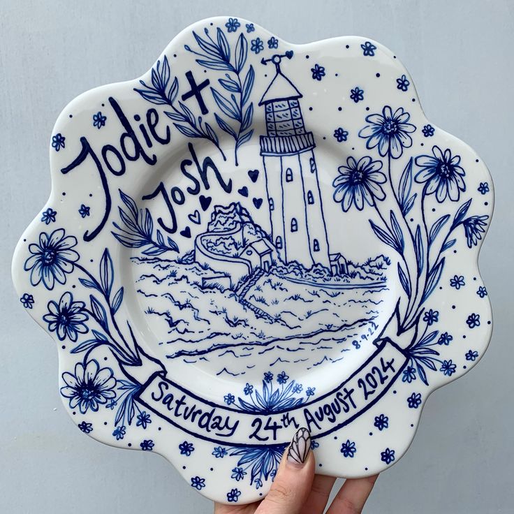 a hand holding a blue and white plate with a lighthouse on it that says jolie & john