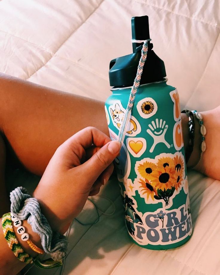 a person holding onto a green water bottle with flowers and hearts on it while laying on a bed