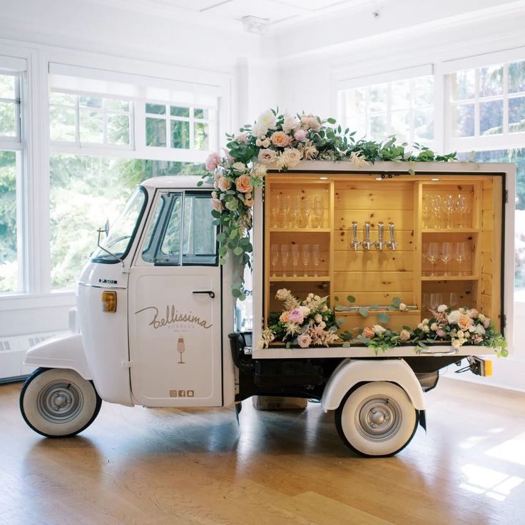 an old truck with flowers and wine glasses in the back is decorated with greenery