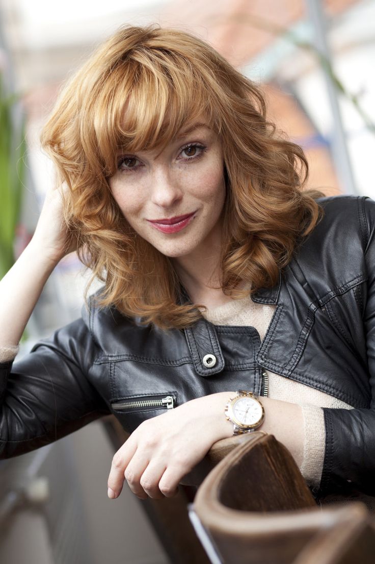 a woman with red hair wearing a black leather jacket sitting at a table and posing for the camera