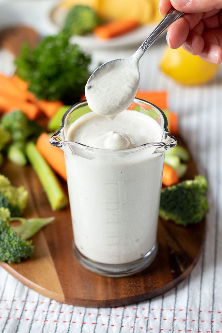 a spoon full of yogurt sitting on top of a wooden plate next to broccoli and carrots