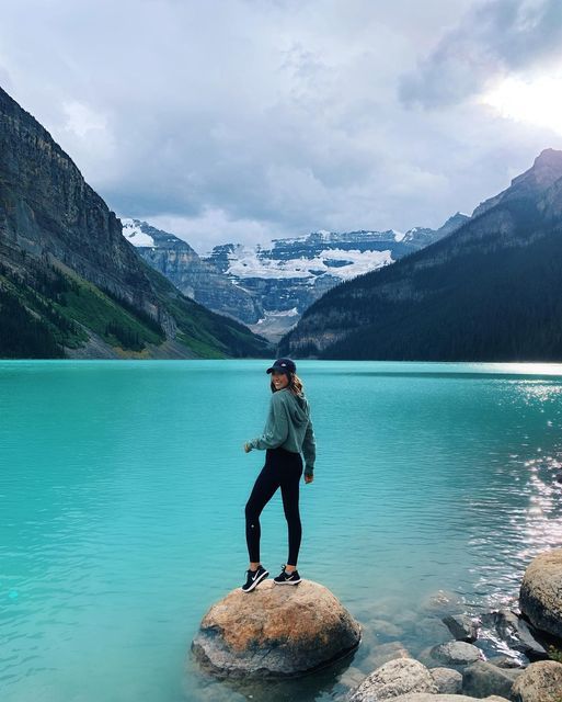 a woman standing on top of a rock in the middle of a lake