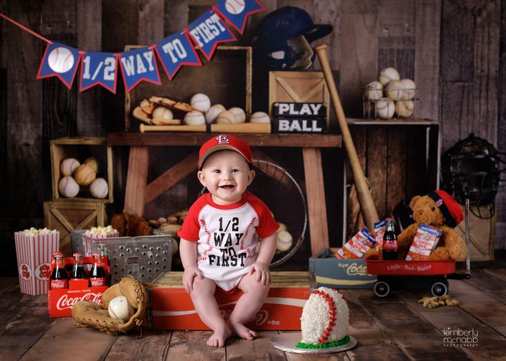 a baby boy sitting on the floor in front of baseball themed cake and other items