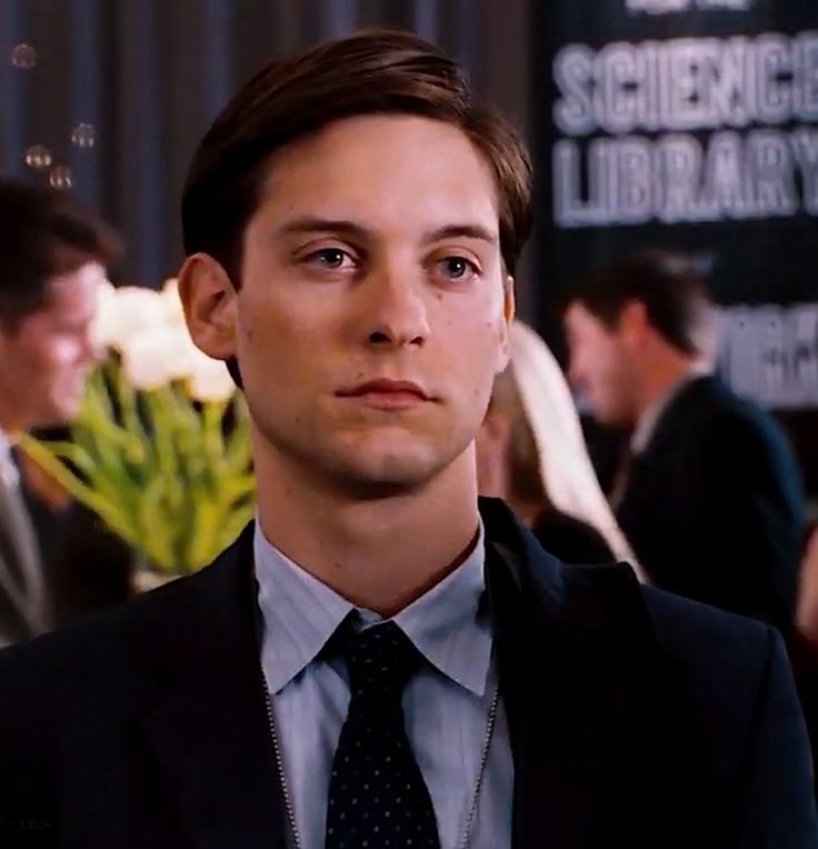 a young man in a suit and tie looking at the camera with other people behind him