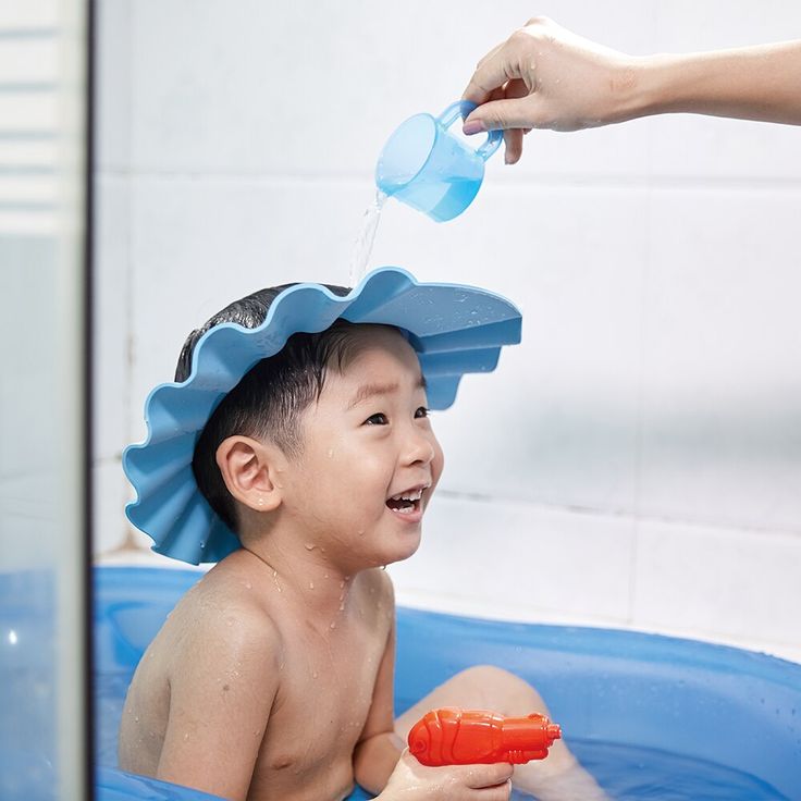 a young boy sitting in a bathtub while being bathed by an adult