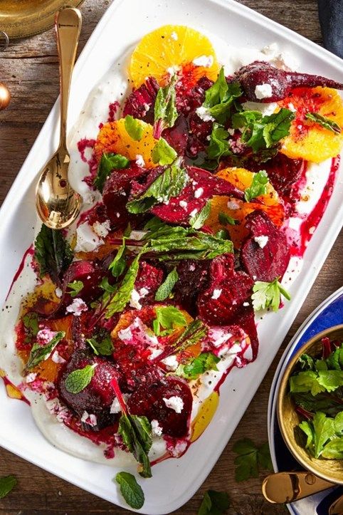 a white platter filled with food next to a bowl of salad and two gold spoons