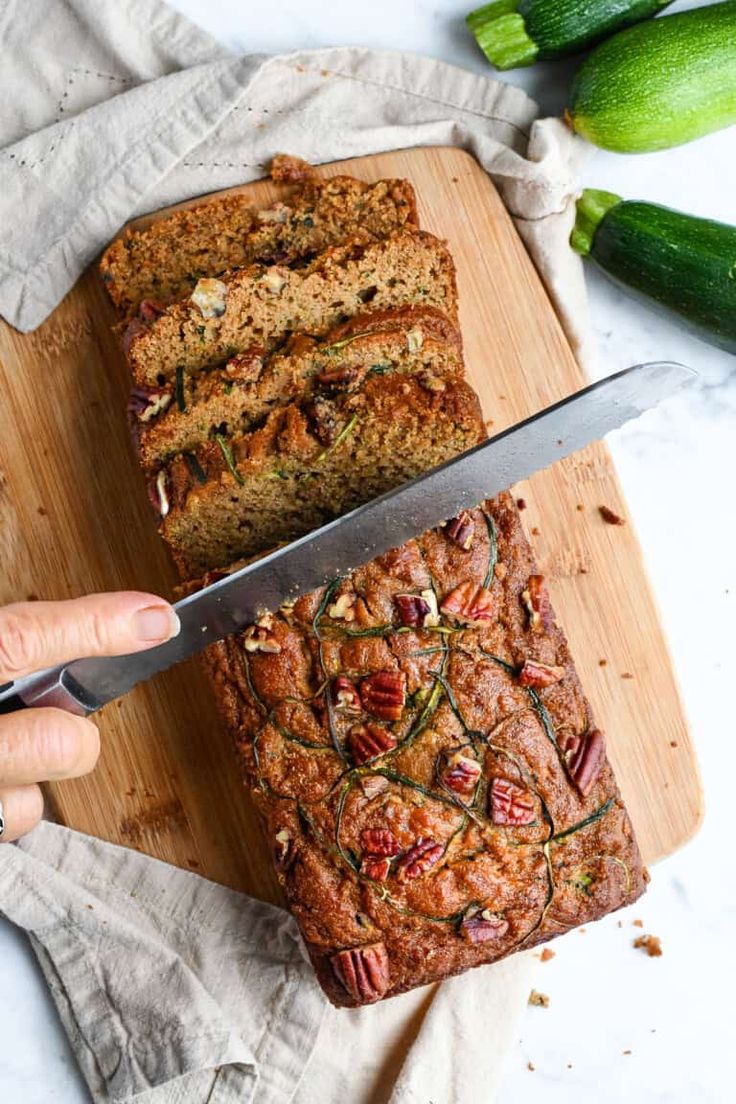 someone is cutting into a loaf of zucchini bread on a wooden cutting board