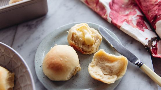 three rolls on a plate with a knife and tins next to them, one half eaten