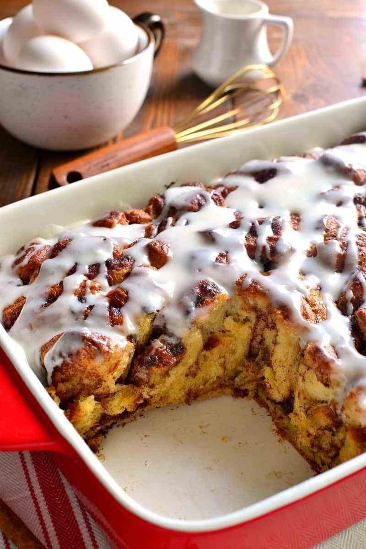 a red casserole dish filled with cinnamon rolls covered in white icing and drizzle