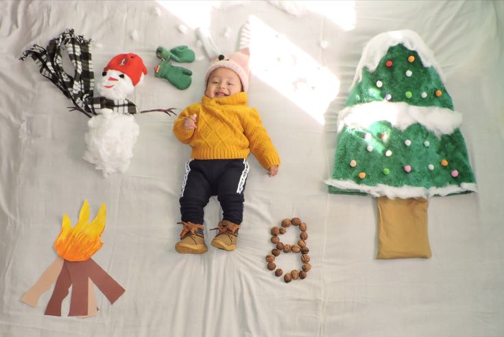 a baby laying on top of a white sheet next to christmas decorations and paper trees