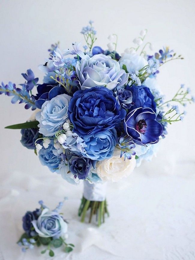 a bridal bouquet with blue and white flowers on a white tableclothed surface