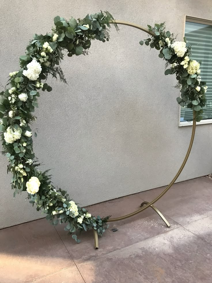 a circular wreath with white flowers and greenery on the side of a building in front of a window