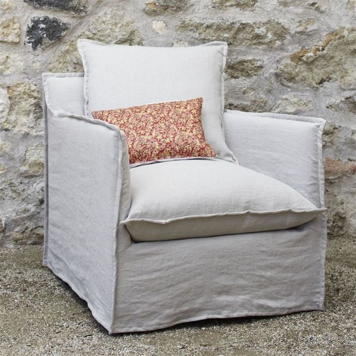 a white chair with a pillow on top of it next to a stone wall and floor