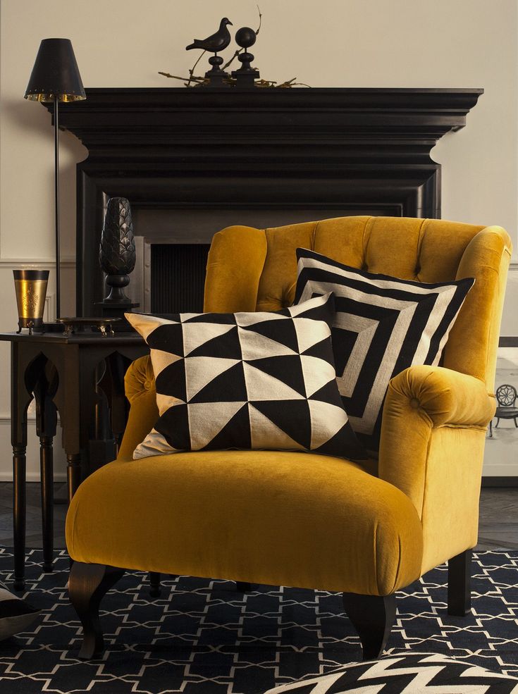 a yellow chair with black and white pillows on it in front of a fire place