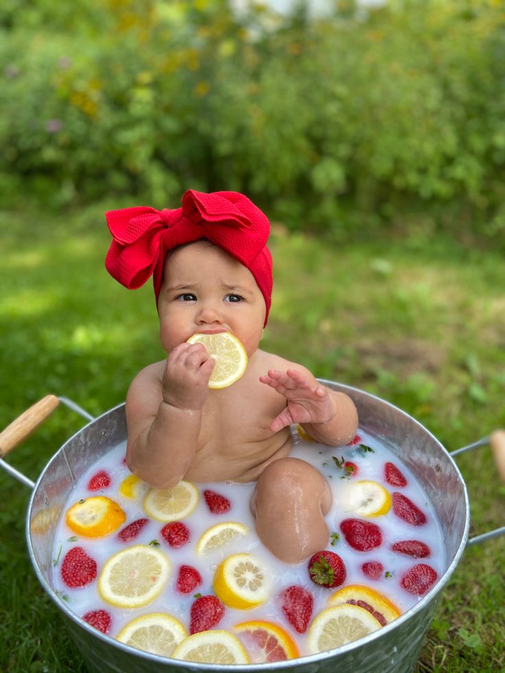 a baby sitting in a tub with lemons and strawberries on it's face