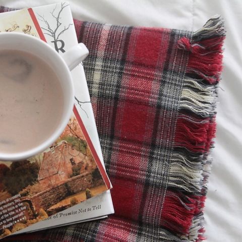 a cup of coffee sitting on top of a bed next to a book and blanket