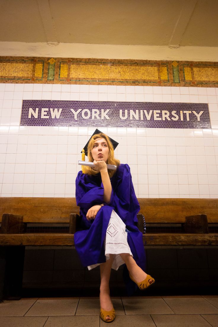 a woman sitting on a bench in front of a new york university sign wearing a cap and gown