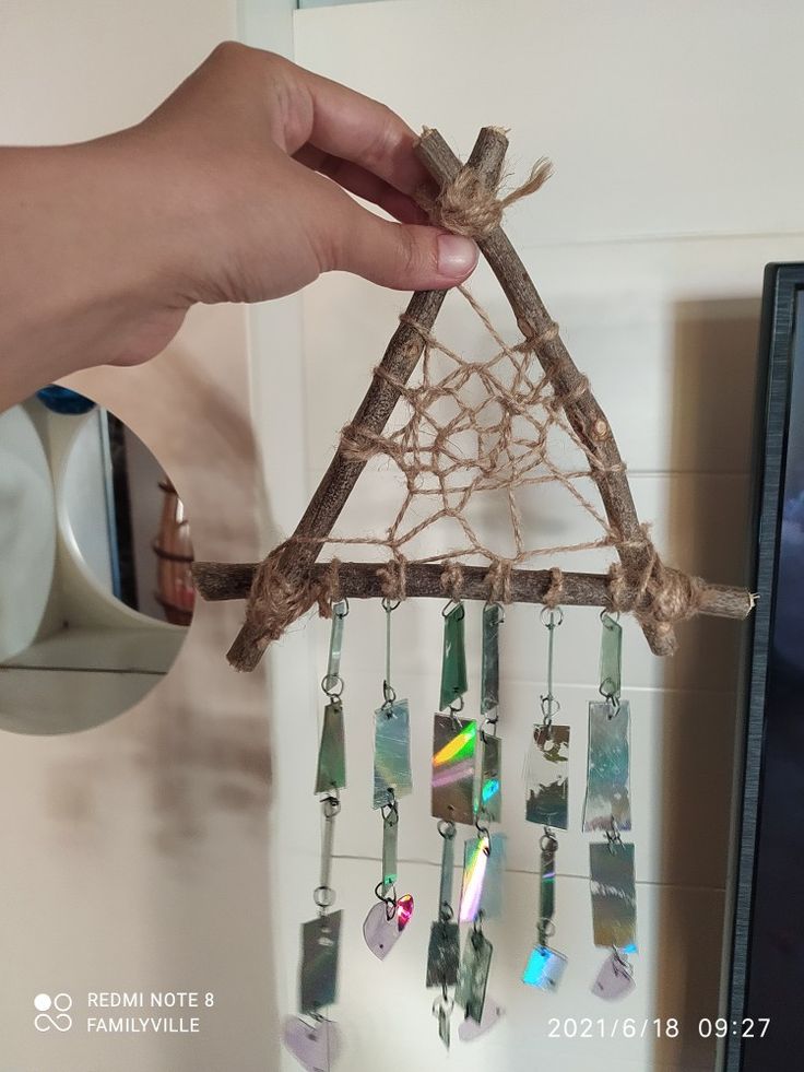 a hand holding a piece of wood with beads hanging from it's side and a triangle made out of sticks