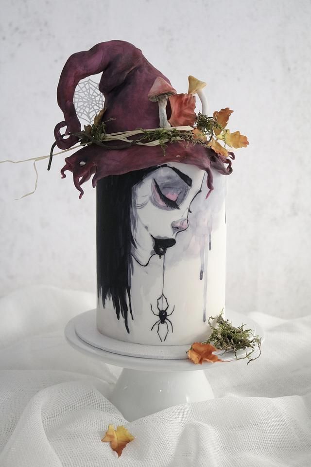 a white and black cup with a witches hat on it's head, surrounded by leaves