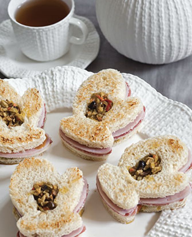 small sandwiches are arranged on a white plate next to a cup of tea and saucer