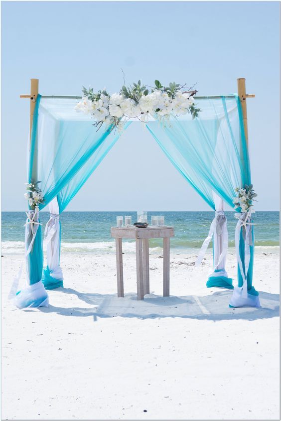 an outdoor wedding setup on the beach with blue draping and white flower arrangements