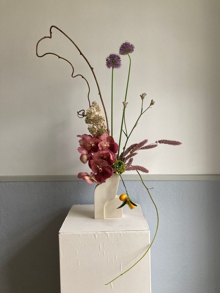 a vase filled with flowers sitting on top of a white box next to a wall