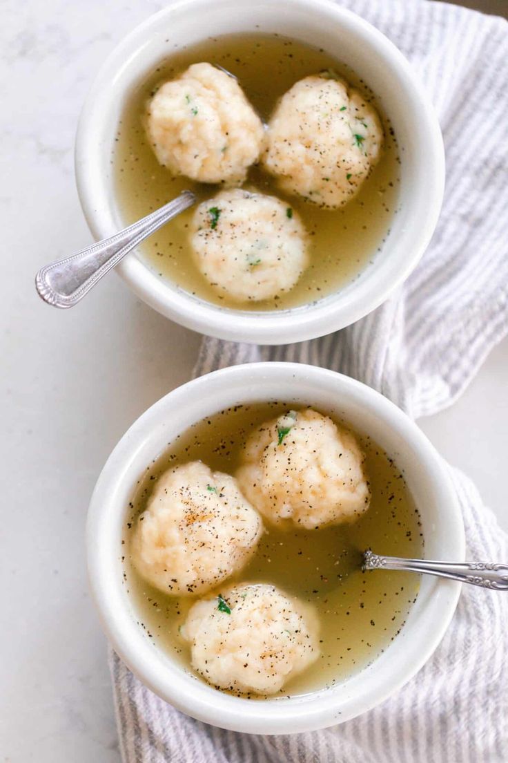 two white bowls filled with dumplings on top of a table next to a spoon