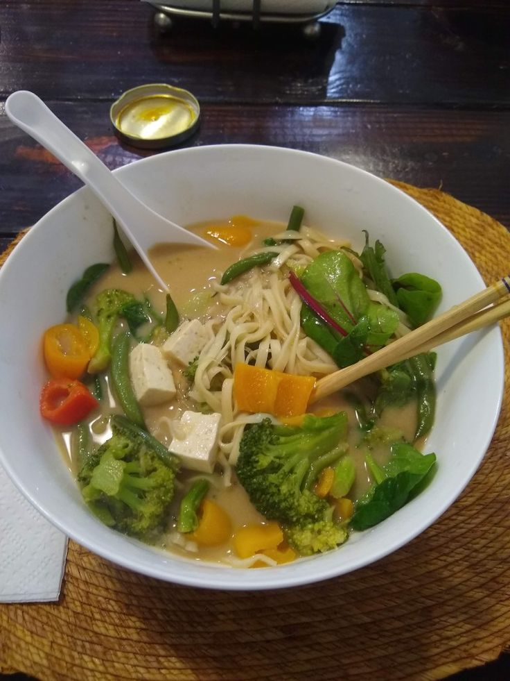 a white bowl filled with noodles, broccoli and carrots on top of a wooden table