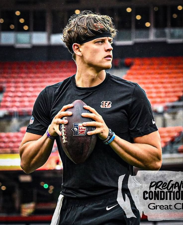 a young man holding a football in his right hand and wearing a black shirt with white lettering on it