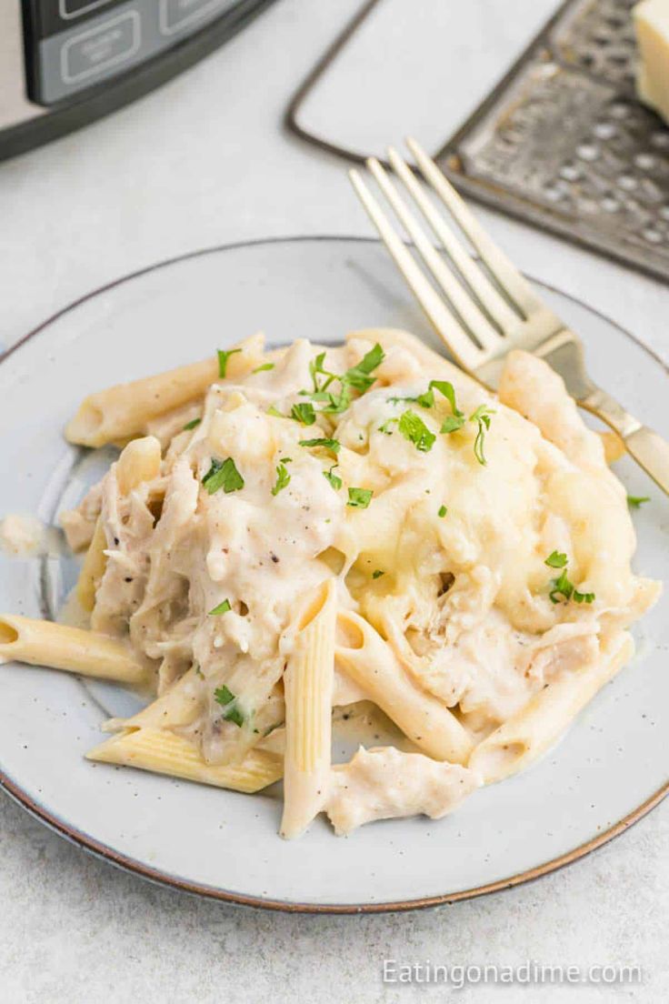 a white plate topped with pasta covered in chicken and sauce next to an instant pressure cooker