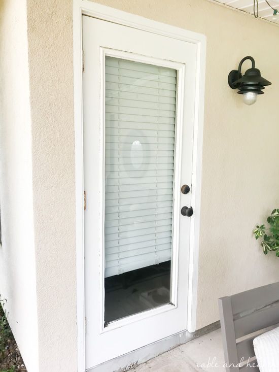 a white door with blinds on it and a bench in front of the door outside