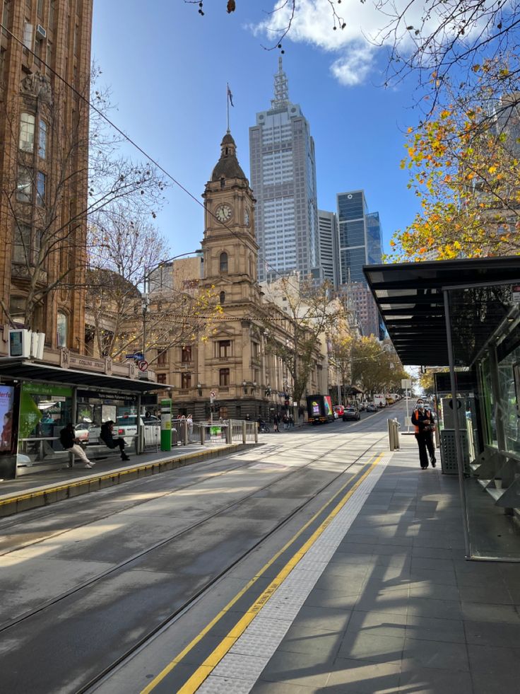 an empty city street with tall buildings in the back ground and people walking on the sidewalk