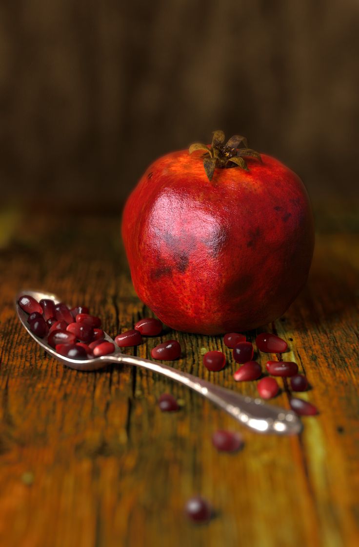 a pomegranate on a wooden table next to a spoon with some seeds