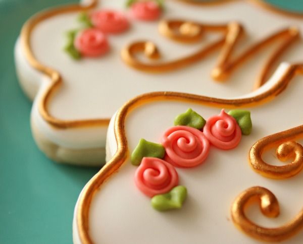 three decorated cookies sitting on top of a blue plate with gold trimmings and roses