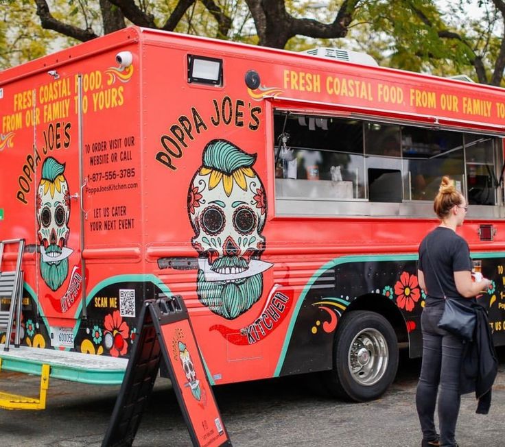 a woman standing in front of a red food truck with skulls painted on the side