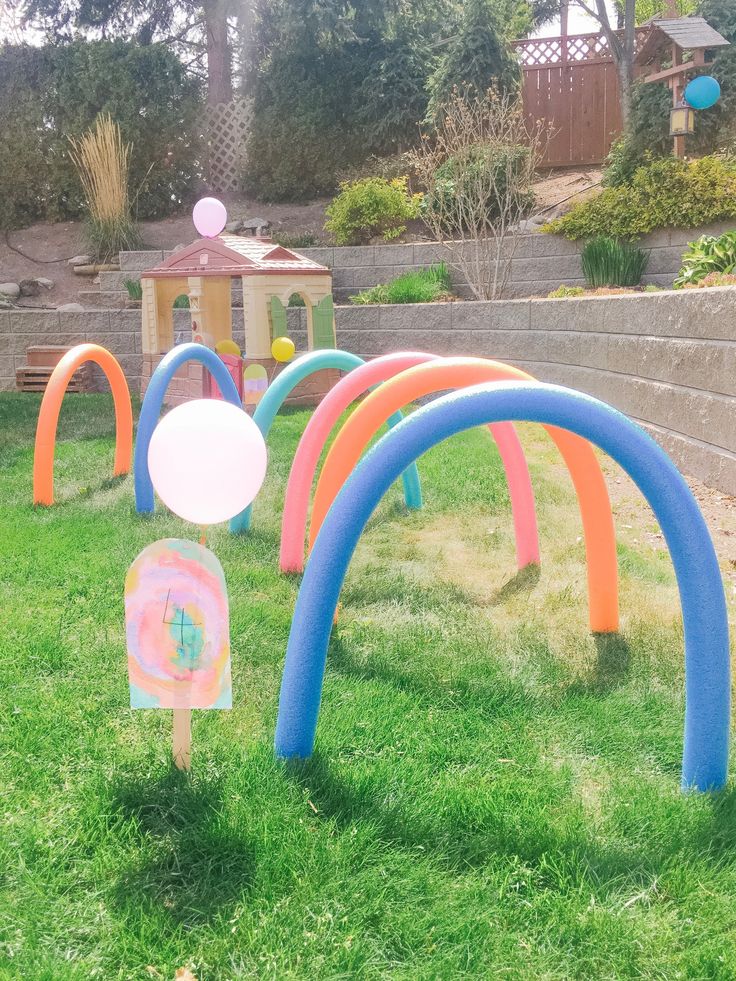 an inflatable arch with balloons and streamers on the grass next to some stairs