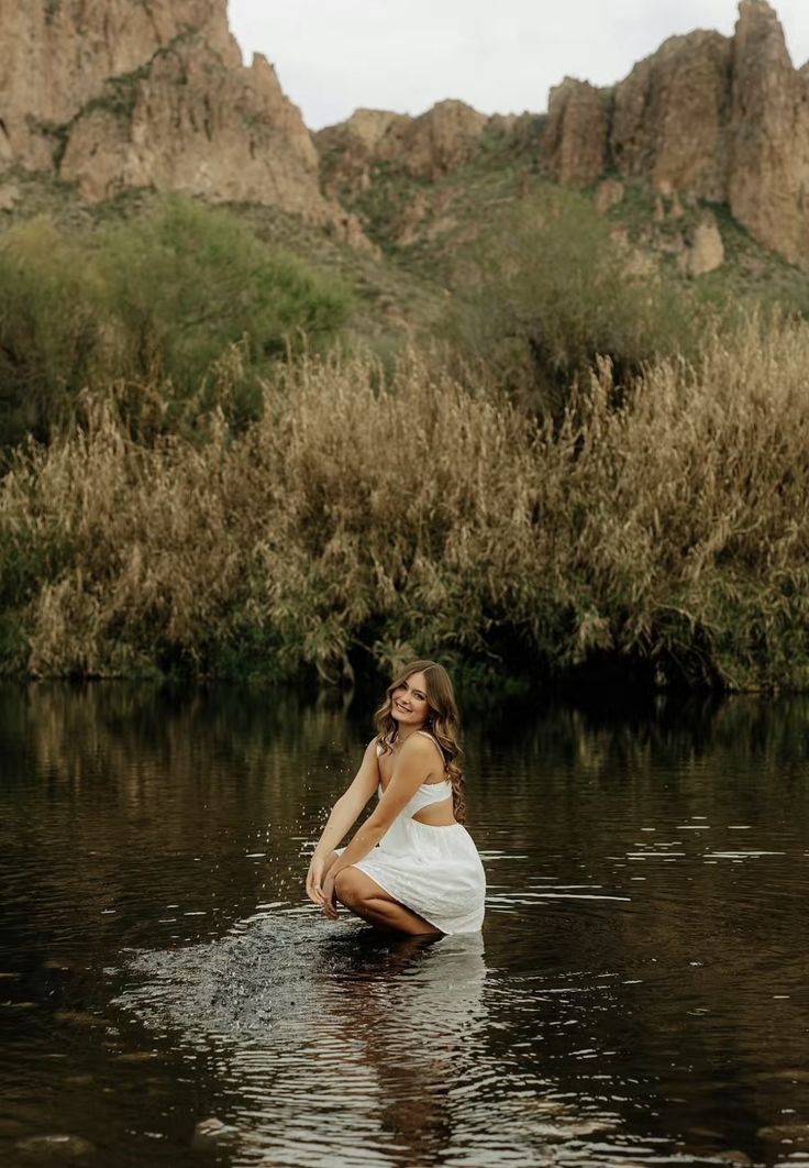 a woman in a white dress sitting on the edge of a body of water