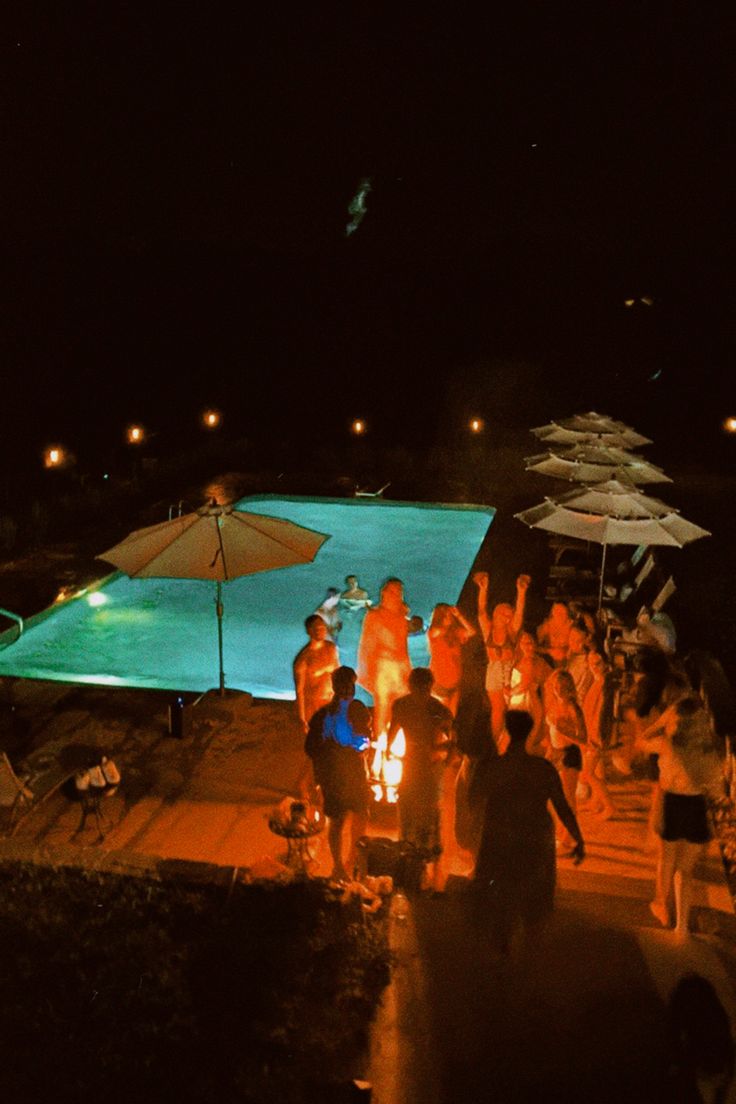 a group of people sitting around a fire pit in the middle of a pool at night