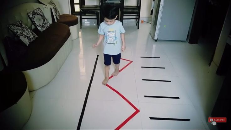 a young boy walking across a white floor with red tape on it's sides