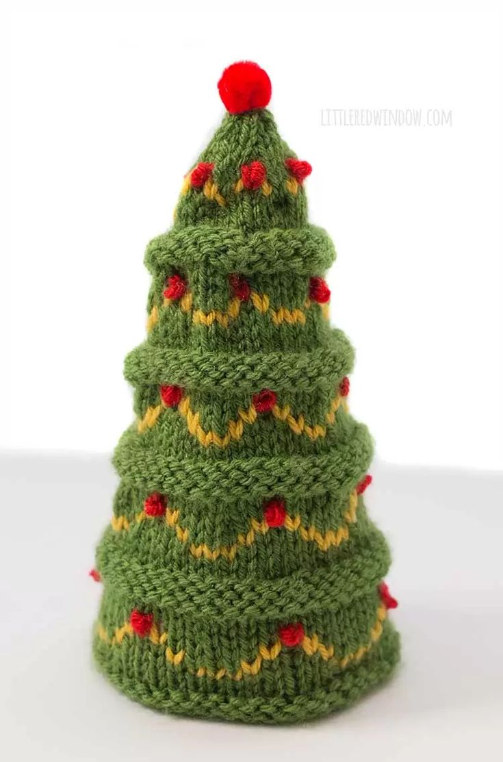 a knitted christmas tree sitting on top of a white table next to a red ball