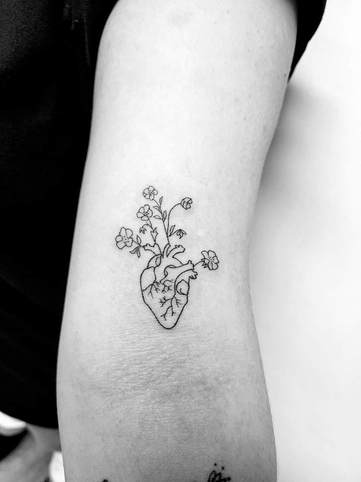 a heart shaped tattoo with flowers on the side of the arm and behind it is an outline of a plant