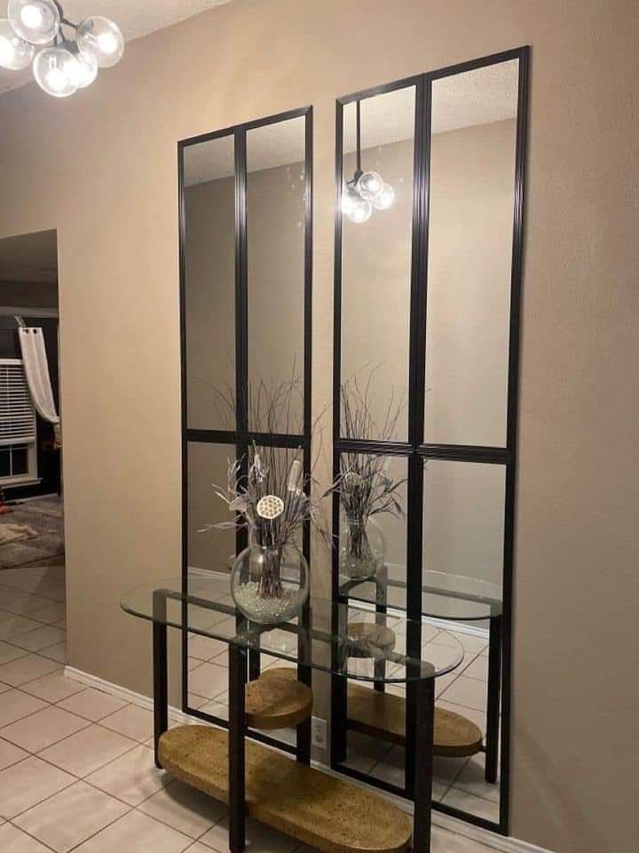 two glass tables with vases and flowers on them in front of a large mirror