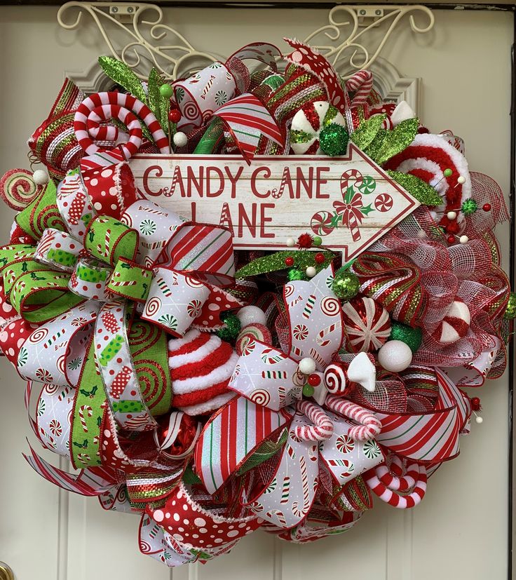 a wreath with candy canes and christmas decorations hanging on the front door to say candy cane lane