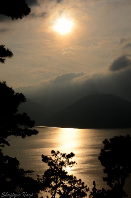 the sun shines brightly through the clouds over a body of water with mountains in the distance