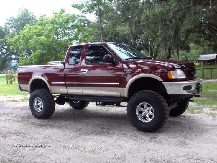 a red pick up truck parked on top of a dirt road in front of trees