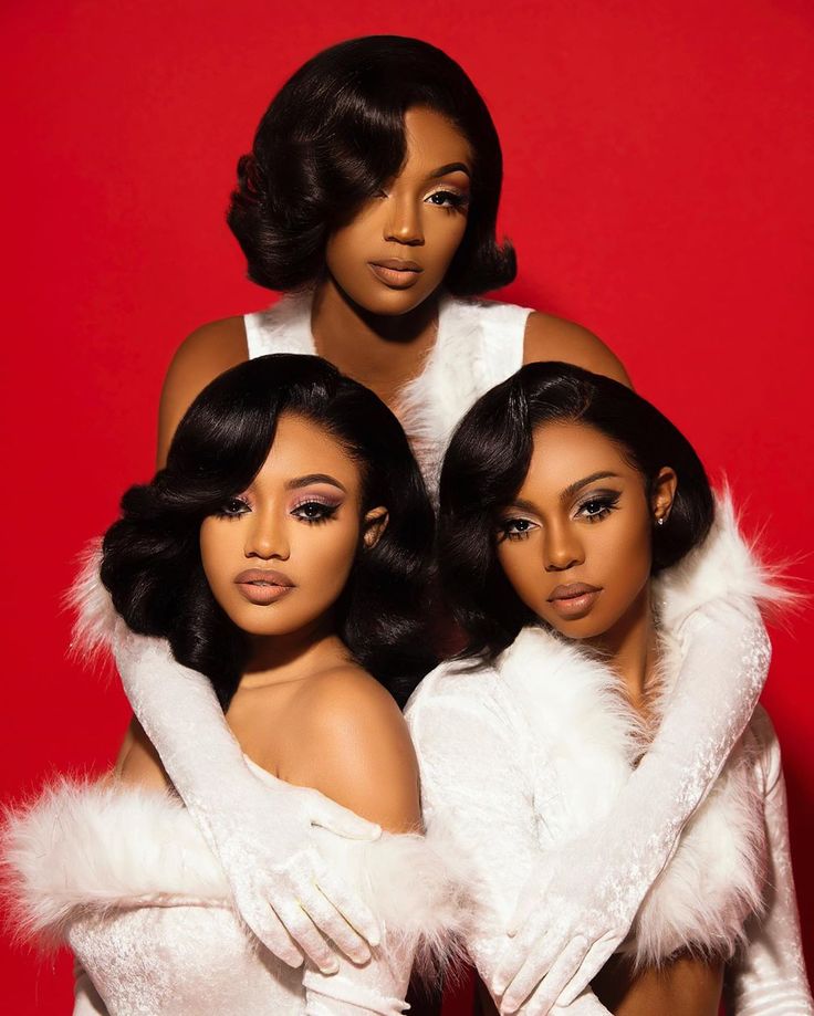 three black women in white fur coats posing for a photo on a red background with their arms around each other