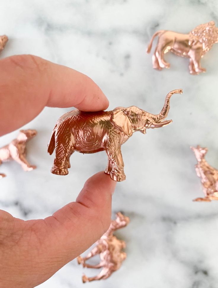 a hand holding a tiny elephant figurine in front of some small elephants on a marble surface