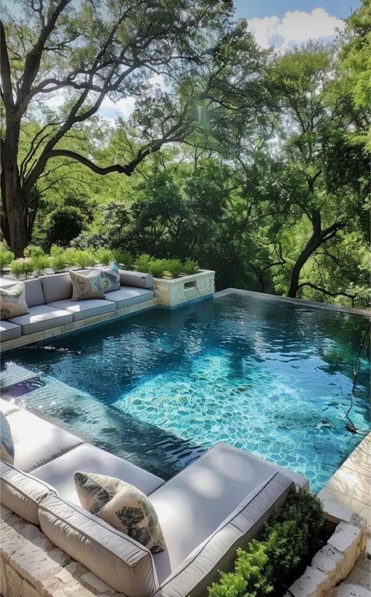 an outdoor swimming pool with couches and trees in the background, surrounded by greenery