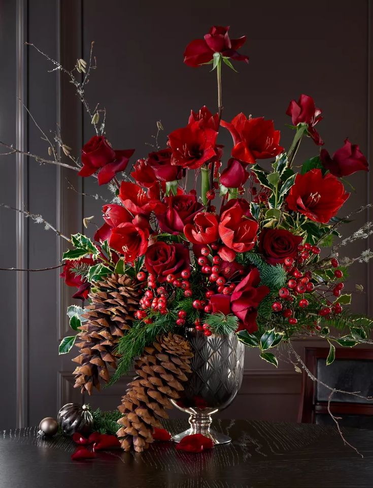 a vase filled with red flowers sitting on top of a table next to a pine cone